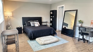 A modern bedroom with a black bed, a desk with a chair, a standing lamp, and a large mirror.