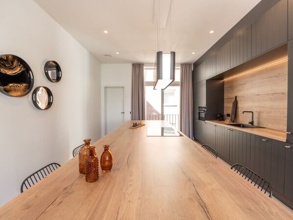 A modern kitchen with a wooden countertop, dark cabinets, and a large dining table.