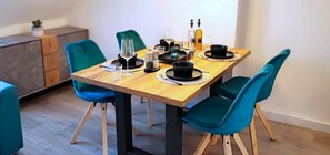 Comedor con mesa de madera dispuesta para dos personas, sillas color aguamarina y un mueble bajo.