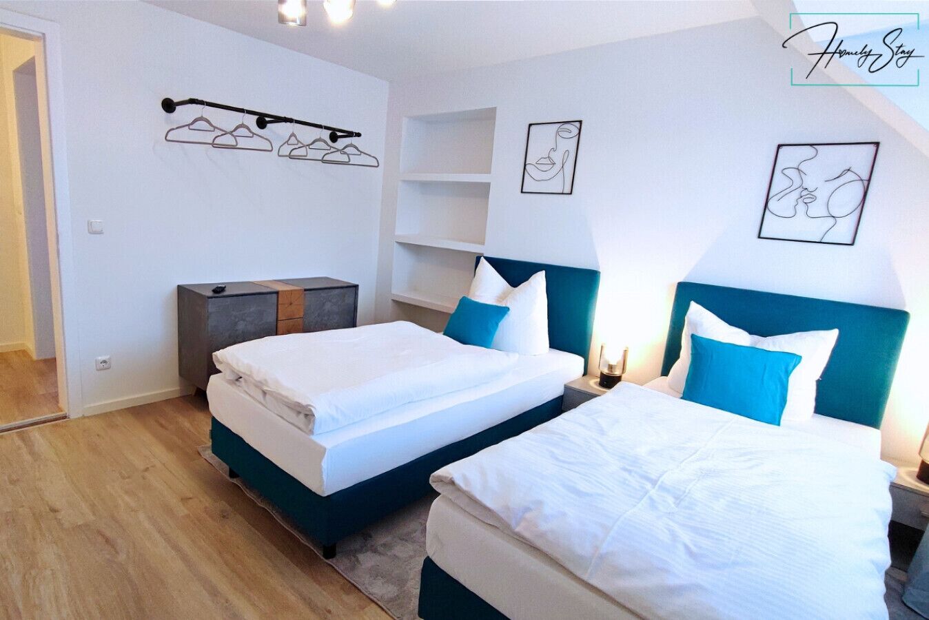 Ein Hotelzimmer mit zwei Betten, einem Kleiderschrank, einem Nachttisch mit Lampe und einem Wandhaken für Kleidung.