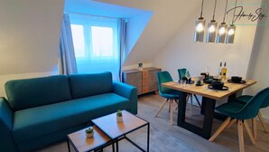 En moderne stue med en turkis sofa, et træbord som sofabord og et spiseområde med et træbord og grønne stole.
