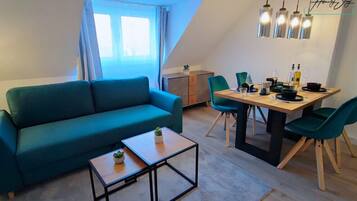 Ein modernes Wohnzimmer mit einem türkisfarbenen Sofa, einem Holztisch und einem Essbereich mit einem Holztisch und grünen Stühlen.