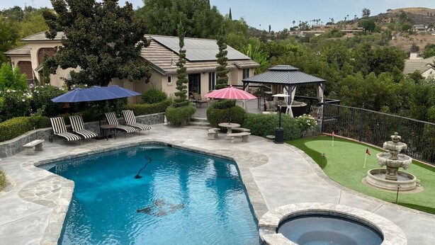 A swimming pool with a hot tub, lounge chairs, and a gazebo.