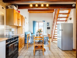 Een kleine keuken met houten kastjes, een eettafel met stoelen, een koelkast en een fornuis.