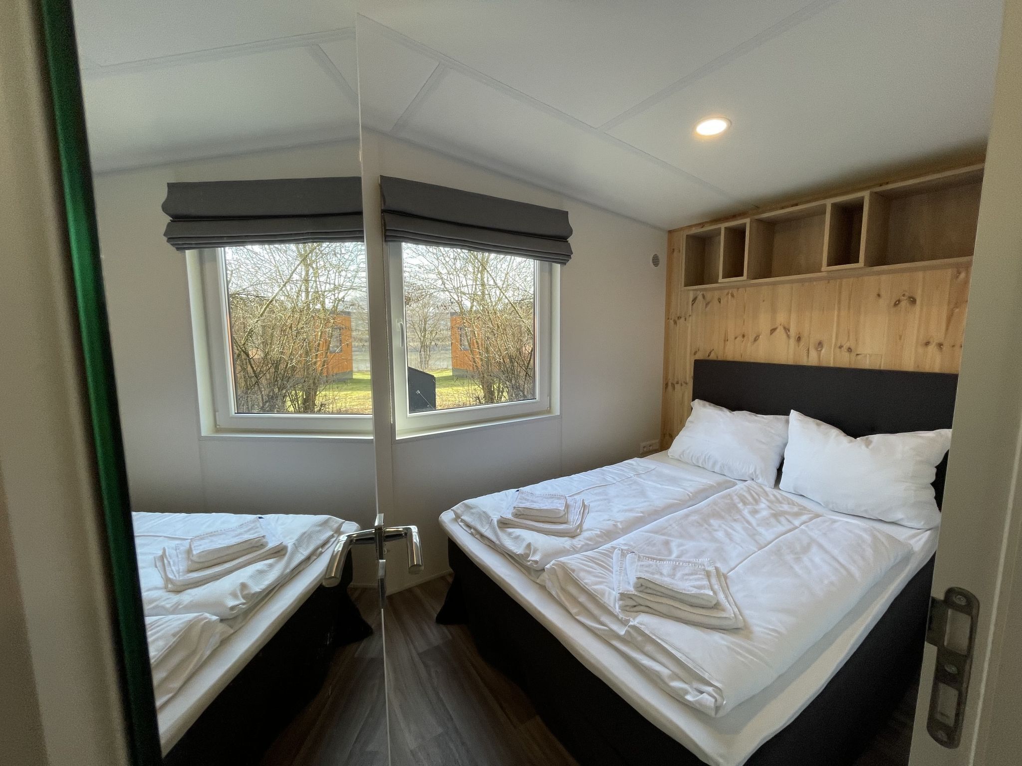A room with two beds, a window with a view of trees, and a wooden headboard.