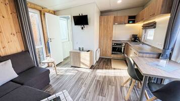 Un espace de vie compact comprenant un canapé, une petite table, un coin cuisine et un téléviseur fixé au mur.