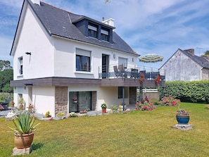 Ein zweistöckiges Haus mit Balkon, Naturstein-Fassade und gepflegtem Garten.