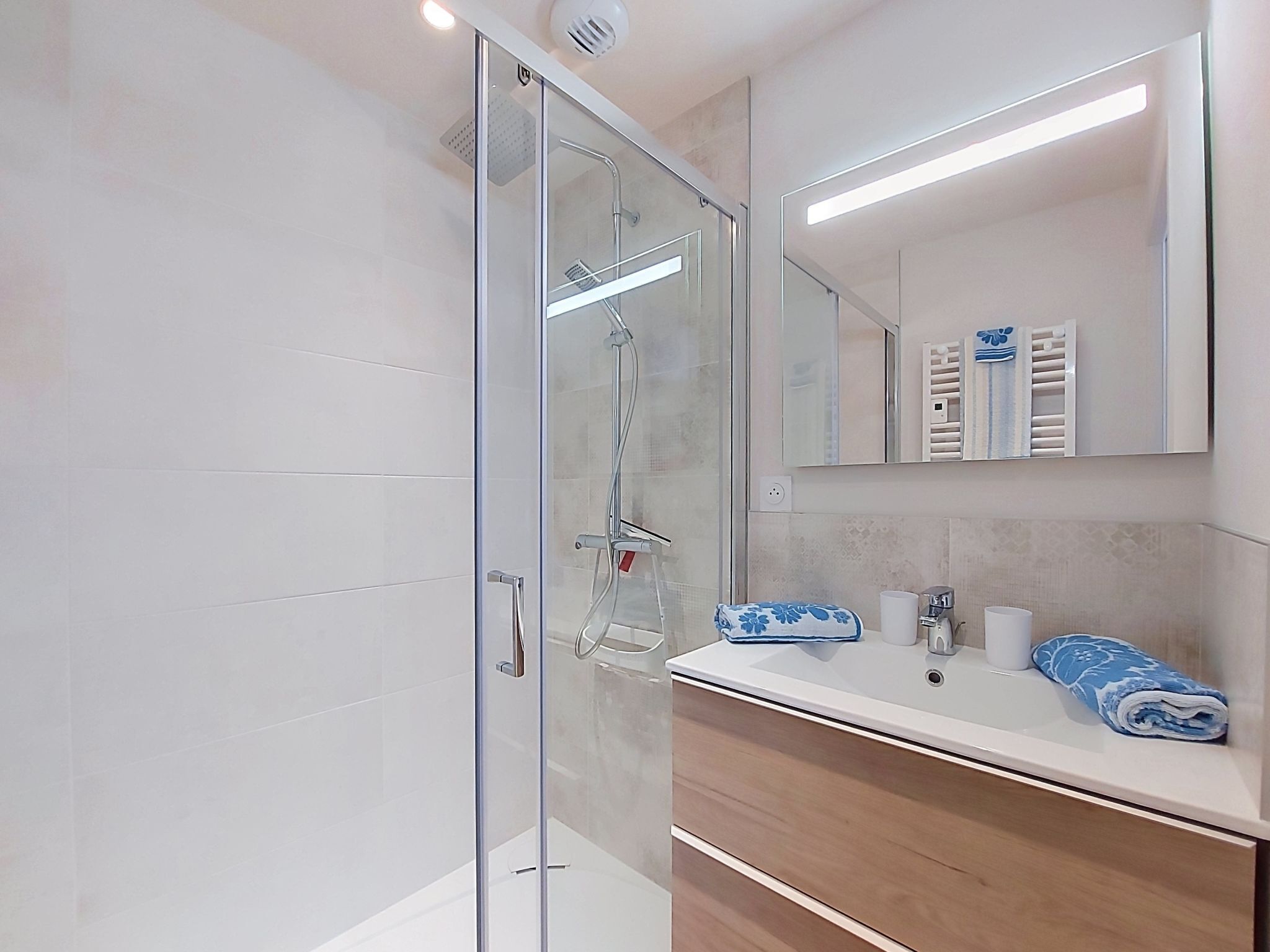 Une salle de bain moderne avec une douche à parois de verre, un meuble-lavabo avec un miroir et un porte-serviettes.