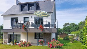 Ein zweistöckiges Haus mit Balkon, einem blumenbewachsenen Garten und einem weißen Zaun im Hintergrund.