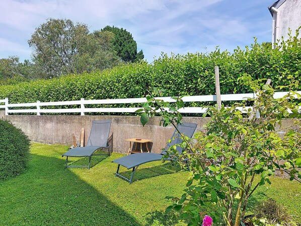 Un jardin avec une clôture blanche, deux chaises longues et une petite table.