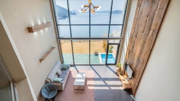 Habitación espaciosa con techos altos y un amplio ventanal con vista a una piscina y una playa.