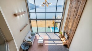 A high-ceilinged room with a large window overlooking a pool and a beach. - Geojedo Raonhiljo Pollvilla Pension (Geoje)