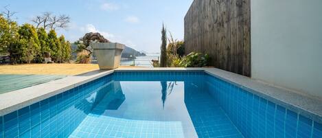 A swimming pool with clear blue tiles, surrounded by a wooden fence and a concrete planter.