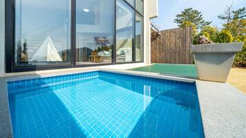 Una piscina con borde de azulejos, cerca de madera y una jardinera de hormigón.