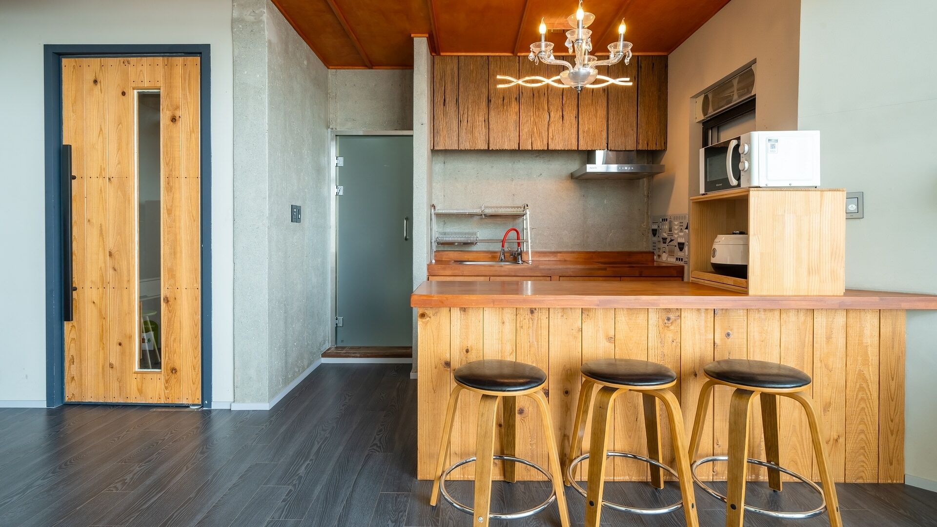 A modern kitchen with wooden cabinetry, a central island with stools, and a chandelier.