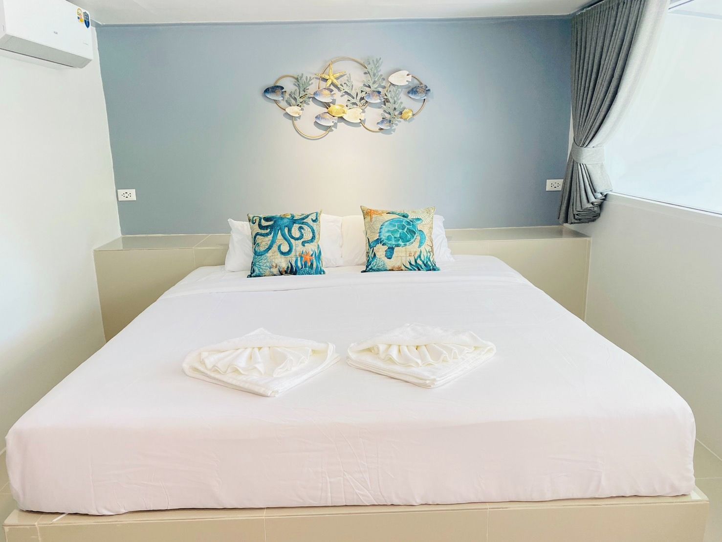 A hotel room with a bed, two pillows, a wall decoration, and a window with curtains.
