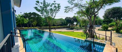 Uma piscina infinita retangular com água azul cristalina, rodeada por um deck de madeira e um guarda-corpo de metal.