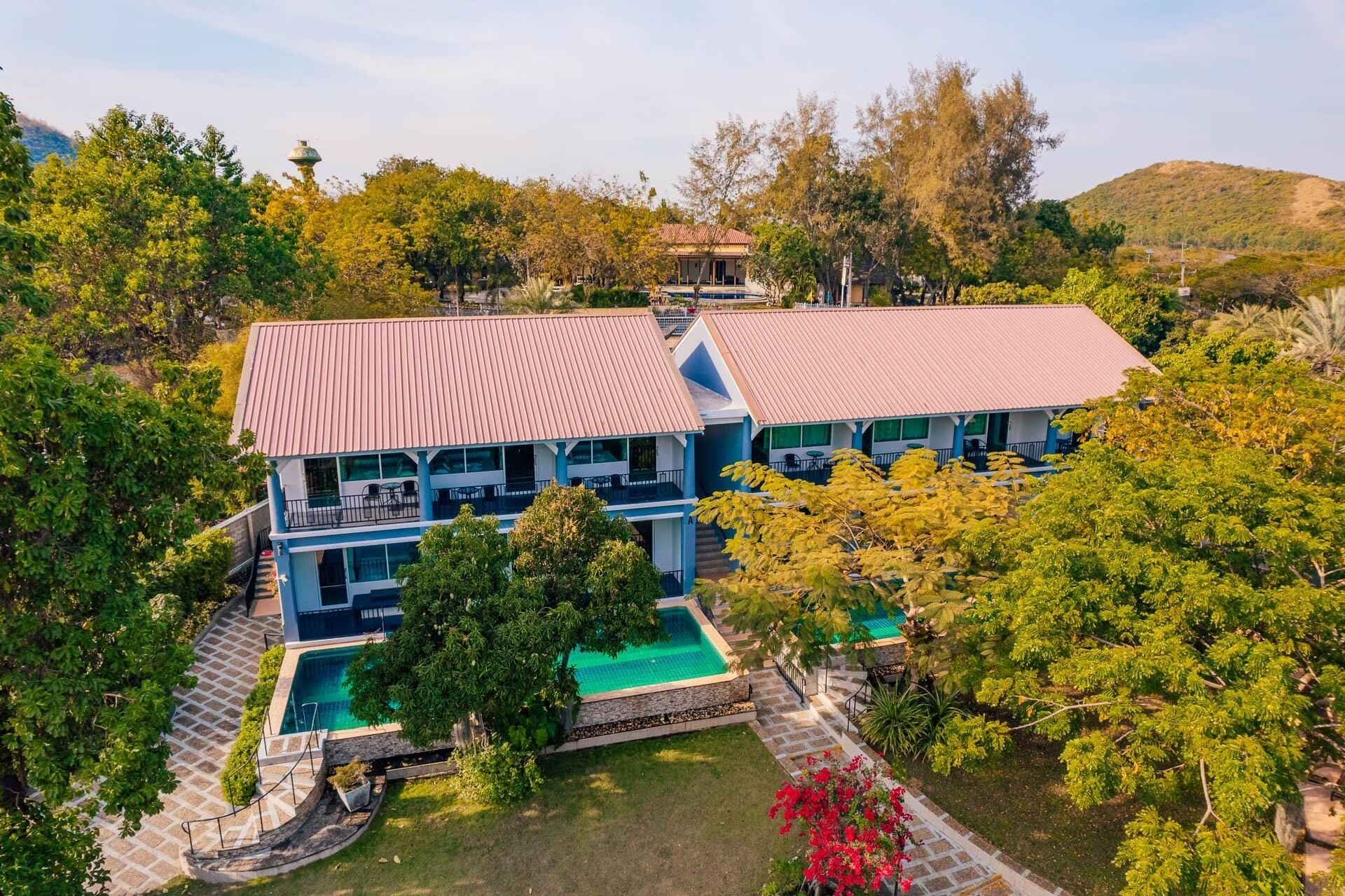 A two-story building with a swimming pool, surrounded by lush greenery and hills.