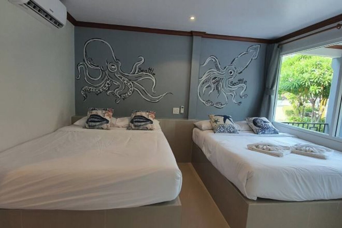 Une chambre d’hôtel avec deux lits, chacun agrémenté de draps blancs et d’oreillers décoratifs. Les murs sont ornés d’œuvres d’art originales représentant des motifs de poulpes et du mot « Seattle ».
