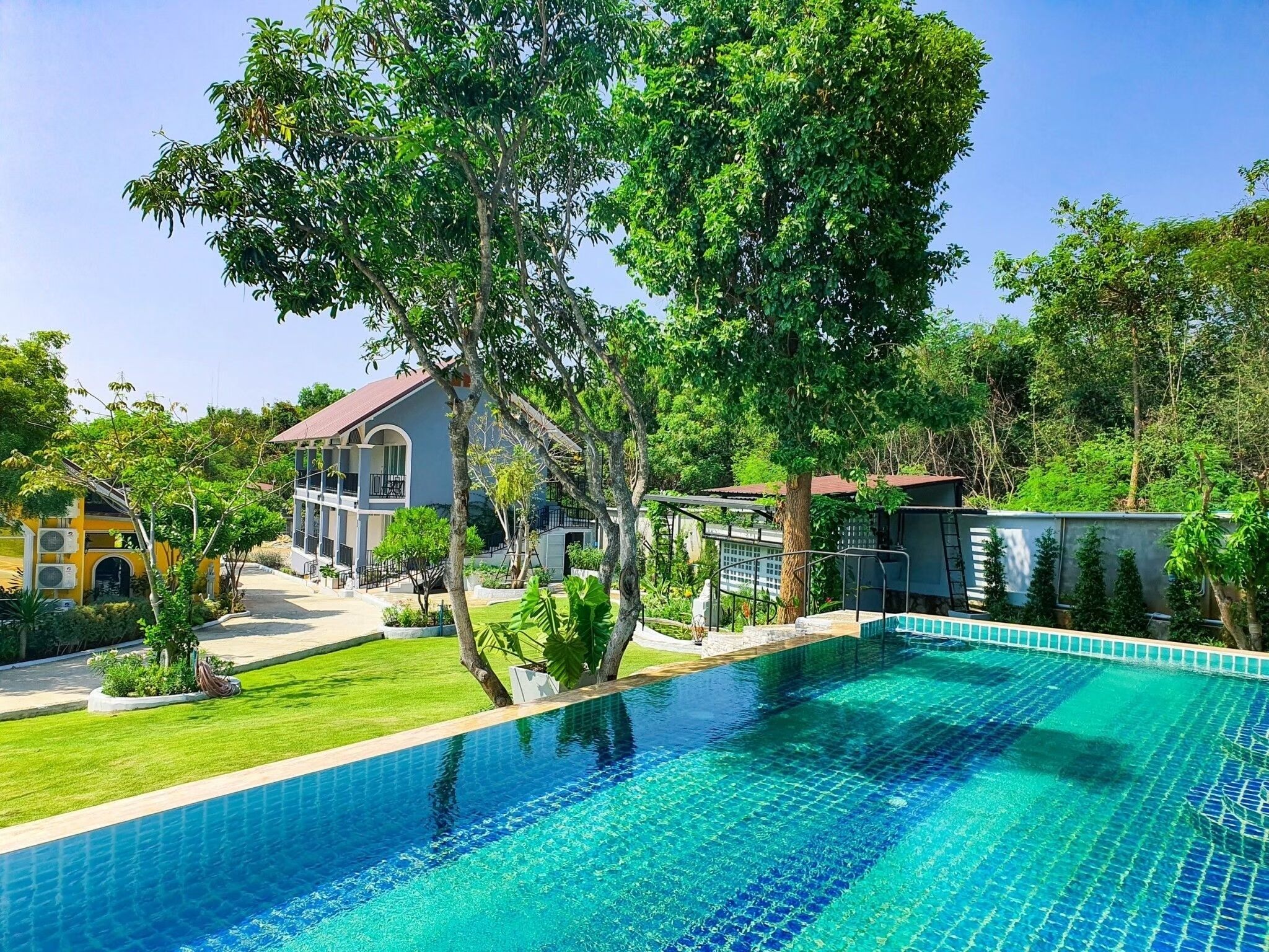 A swimming pool with a tiled edge, surrounded by a well-maintained lawn and trees.