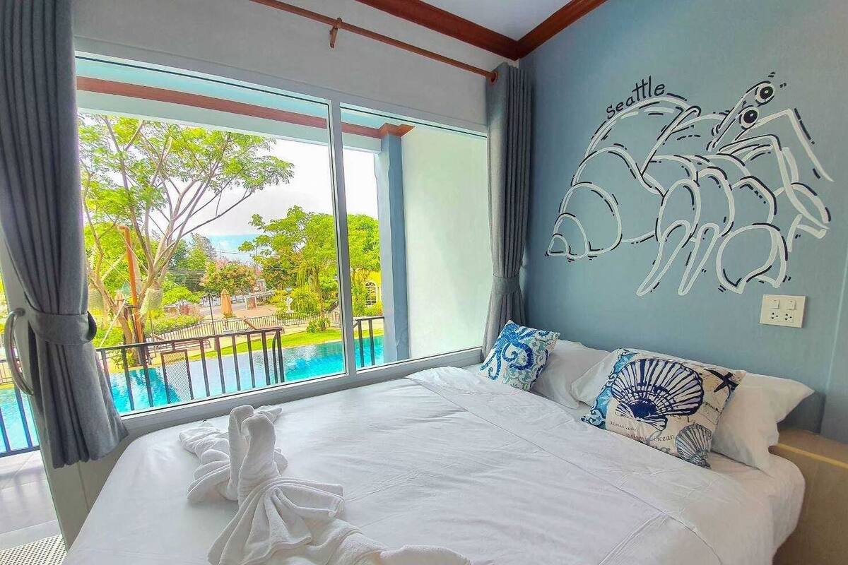 Habitación de hotel con una cama grande, vista a una piscina y un mural de una tortuga marina en la pared.