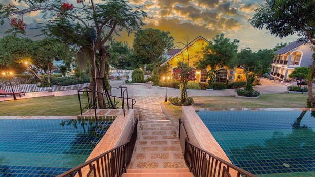 A pool area with a staircase leading to a building, surrounded by greenery and a sunset sky. - Seattle Samaesarn Resort (Sattahip)