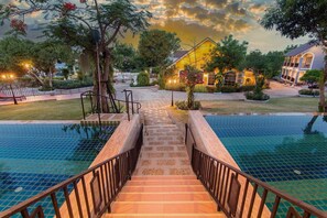 A pool area with a staircase leading to a building, surrounded by greenery and a sunset sky. - Seattle Samaesarn Resort (Sattahip)