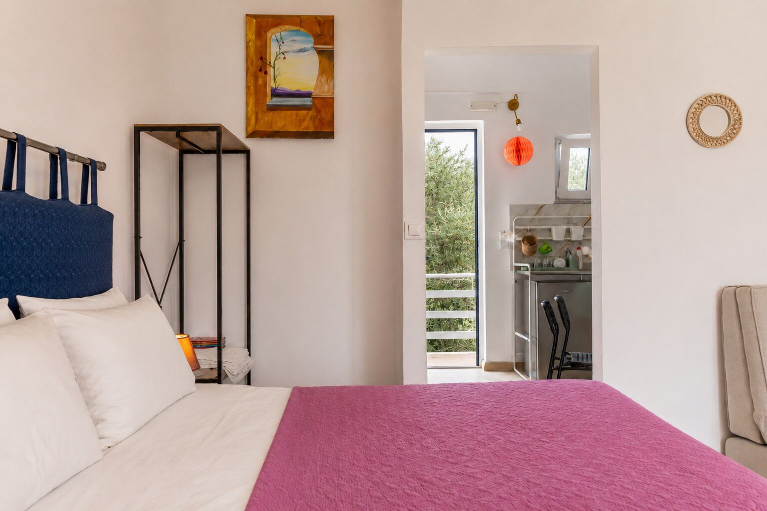Een slaapkamer met een bed, een kledingkast, een schilderij, een kitchenette en een balkon.