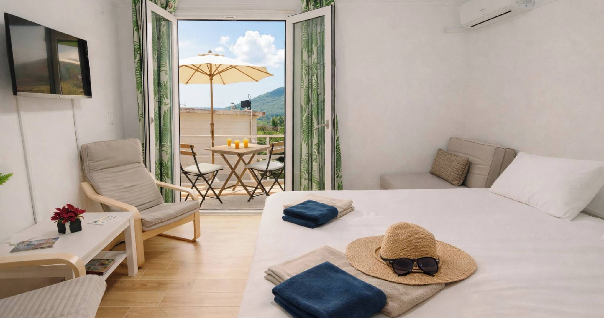 Quarto de hotel com cama, uma cadeira, mesa pequena e varanda com mesa e guarda-sol.