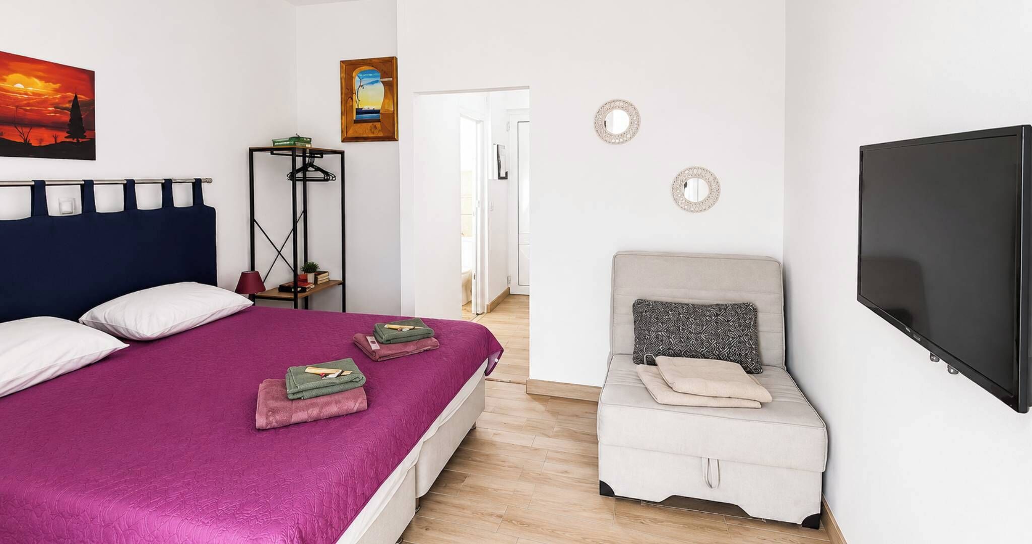 Quarto com uma cama, uma cadeira, uma televisão e um quadro na parede.