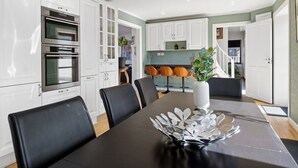Una cocina moderna con gabinetes blancos, electrodomésticos de acero inoxidable y un comedor con mesa y sillas negras.