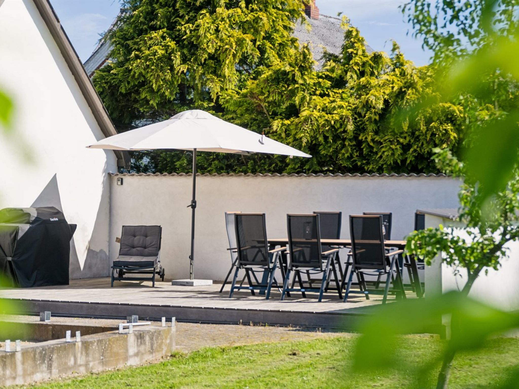 Een terras buiten met een tafel, stoelen, een witte parasol en een barbecue.