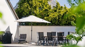 Un patio exterior con una mesa, sillas, una sombrilla blanca y una parrilla.