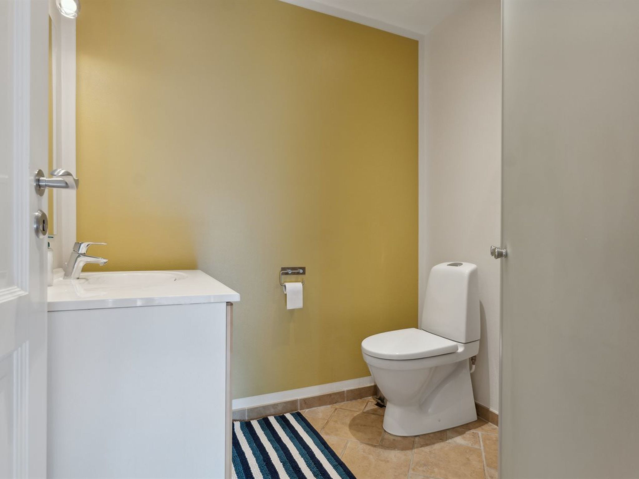 A bathroom with a white sink, a toilet, and a striped rug on the floor.