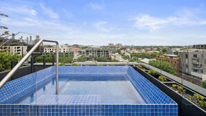 A rooftop pool with blue tiles, surrounded by buildings and a clear sky. - Art Deco Retreat - Hot Tub|Parking (Collingwood)