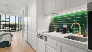 A modern kitchen with white cabinetry, a green backsplash, and a large window overlooking a cityscape. - Art Deco Retreat - Hot Tub|Parking (Collingwood)