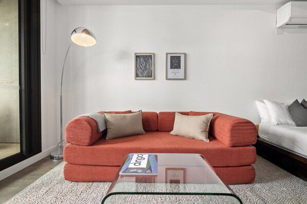 A modern living room with a red sofa, a glass coffee table, and two framed artworks on the wall. - Modern, Industrial Hideaway (Collingwood)