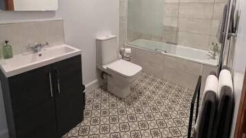 Un baño con lavamanos blanco, gabinete oscuro, inodoro, ducha y piso estampado.
