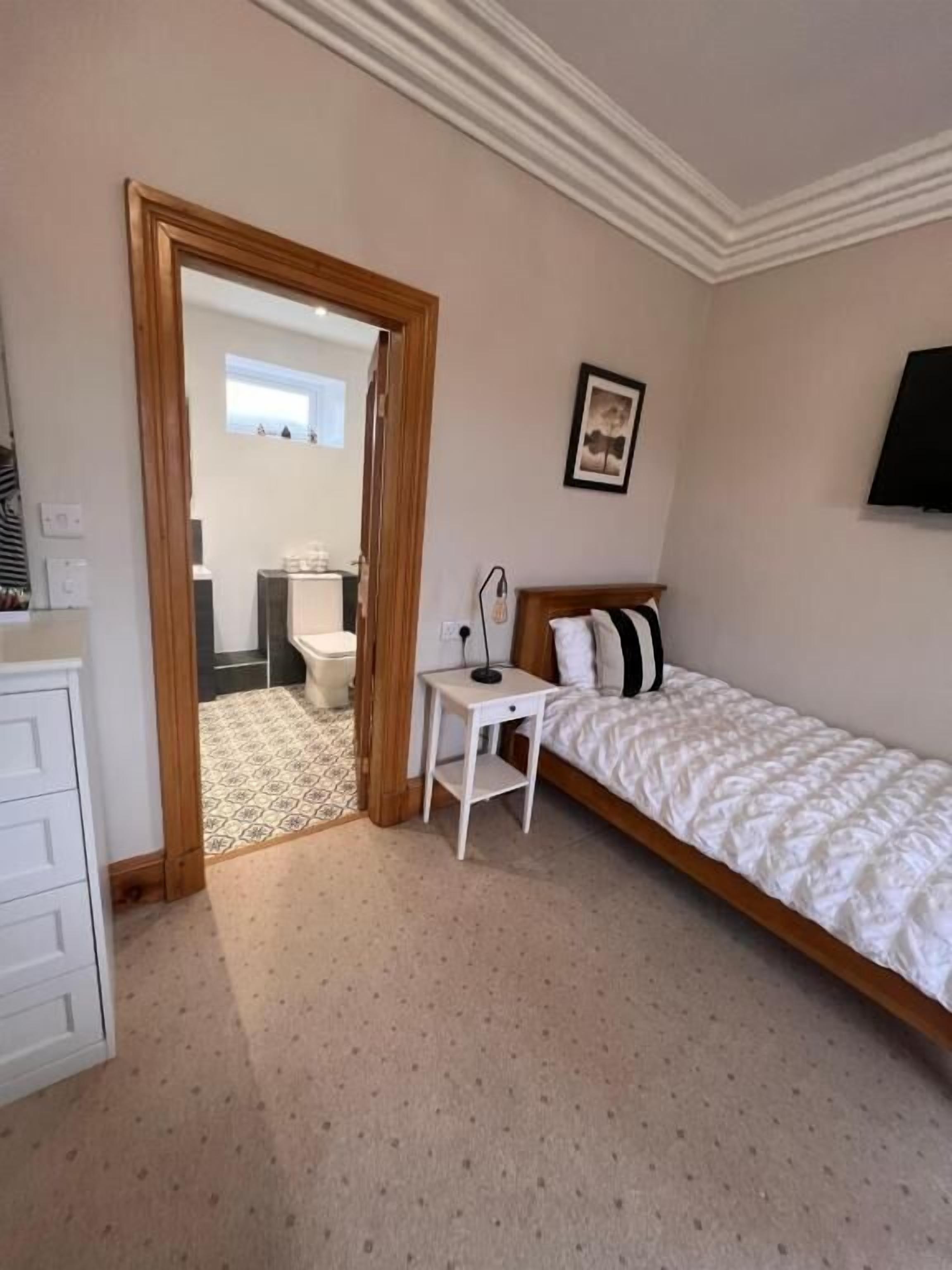 A bedroom with a bed, a small desk, a chair, and a wardrobe.