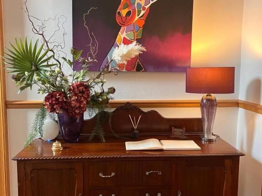 A wooden desk with a vase of flowers, a lamp, and a painting of a giraffe on the wall.