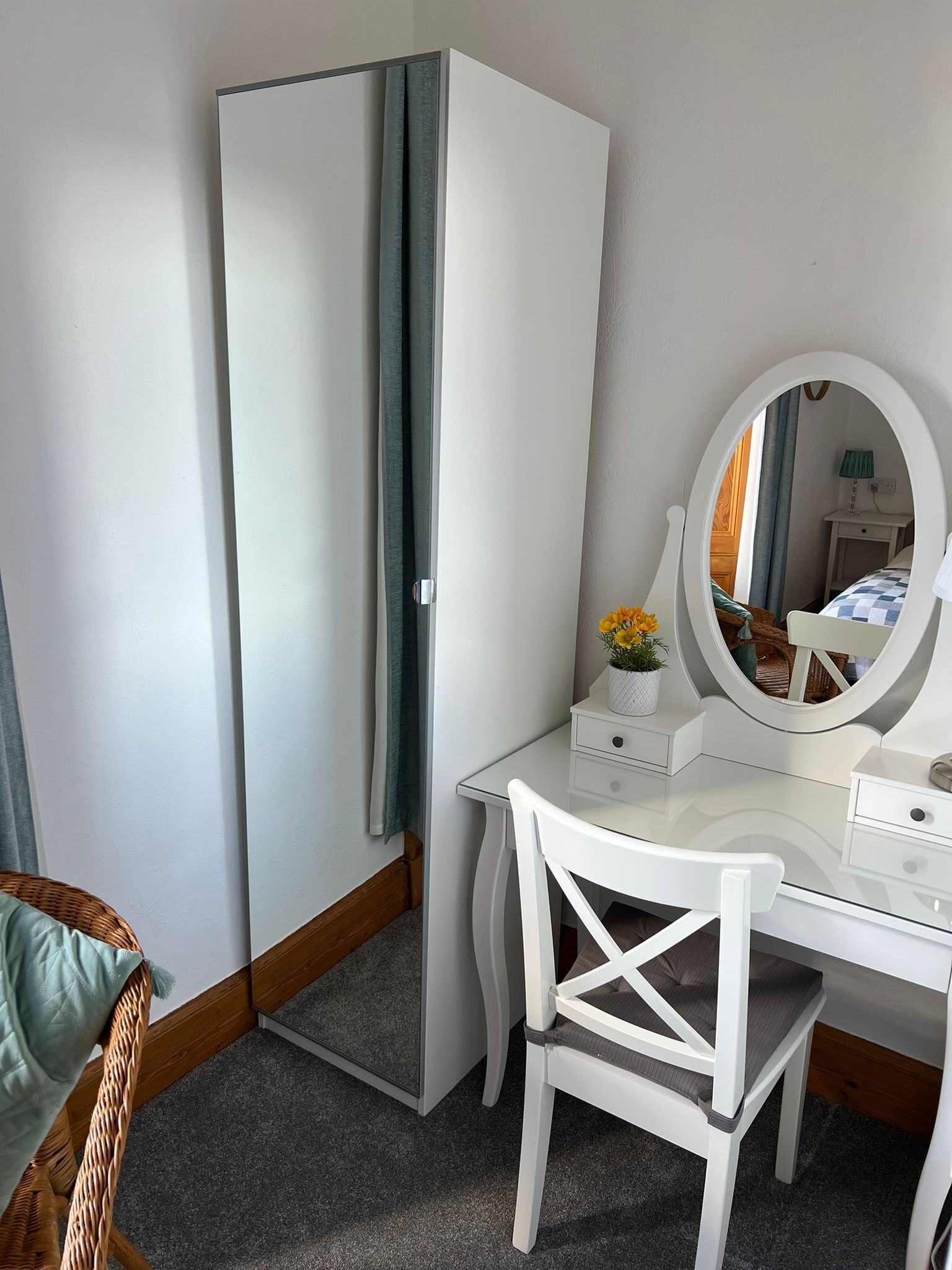 Un dormitorio pequeño con un armario blanco, un escritorio con espejo y una silla de mimbre.