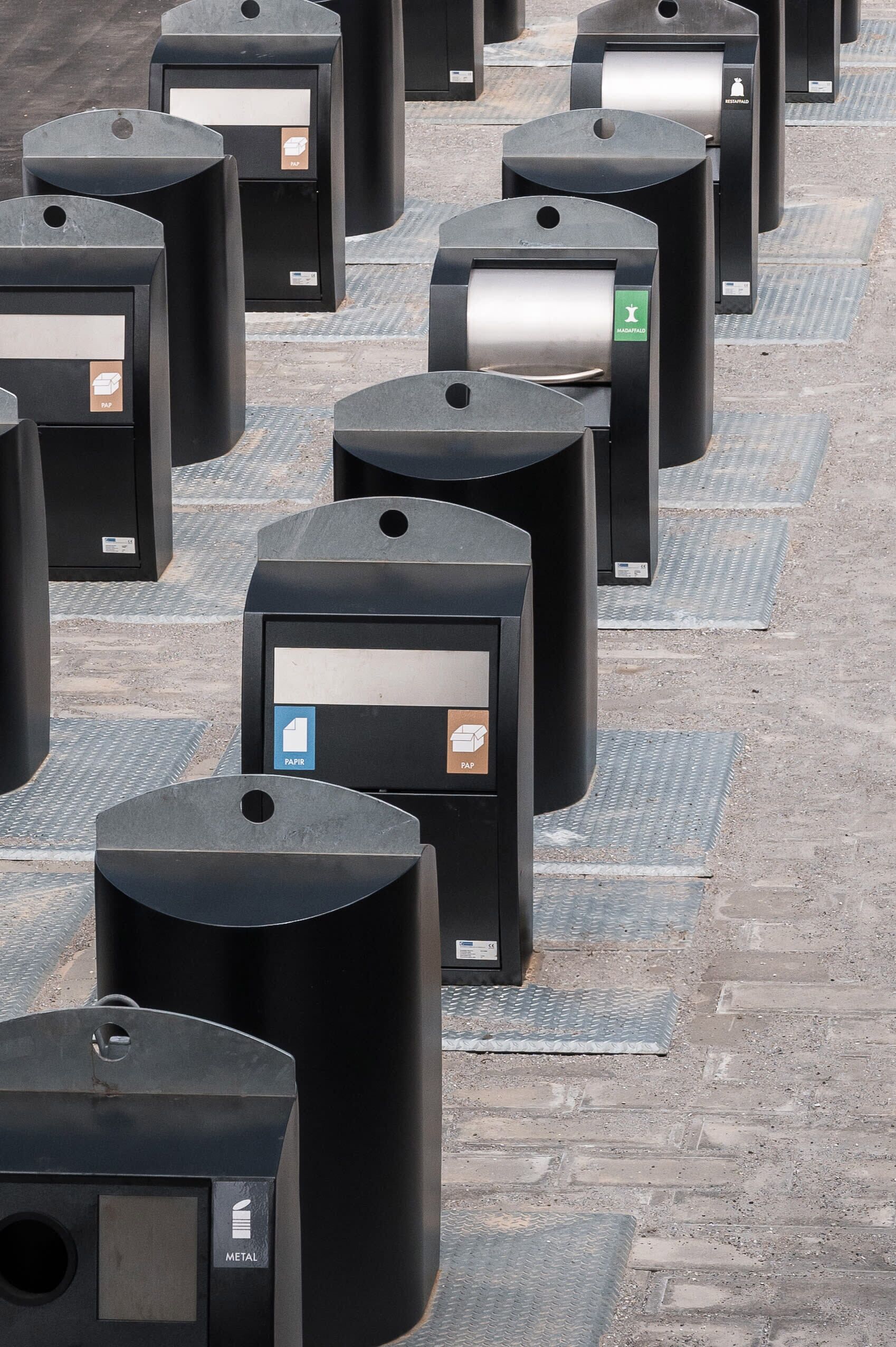 Une rangée de poubelles noires, chacune portant une étiquette indiquant le type de déchets à y déposer.