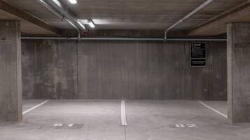 An empty parking garage with concrete walls and floors, marked parking spaces, and overhead fluorescent lighting.
