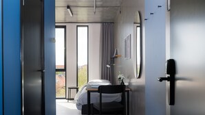 Camera d'albergo moderna con un letto, una scrivania e una sedia. Una finestra con tende offre vista all'esterno.