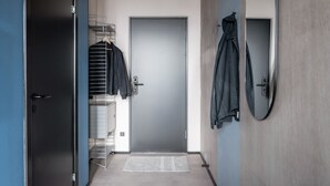 A hallway with a closed door, a coat rack with jackets, and a small rug on the floor.