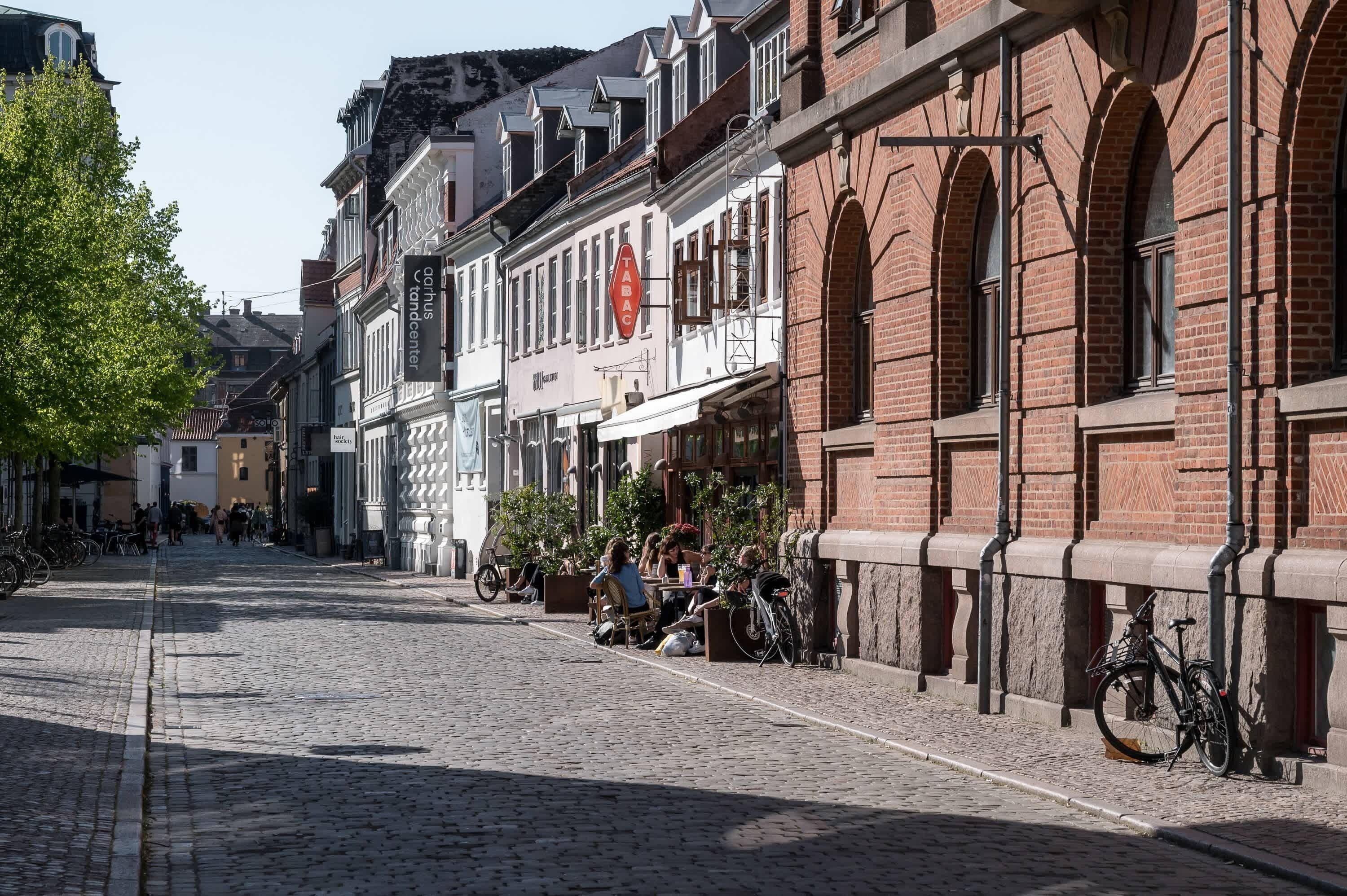 A cobblestone street lined with historic buildings, including a tobacconist and a café.