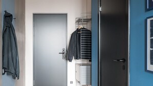 Un pasillo con una puerta cerrada, un perchero con ropa colgando y una pared azul.