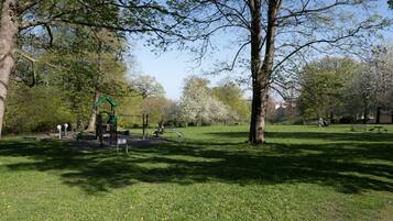 Un parque con un área de juegos, bancos y árboles.