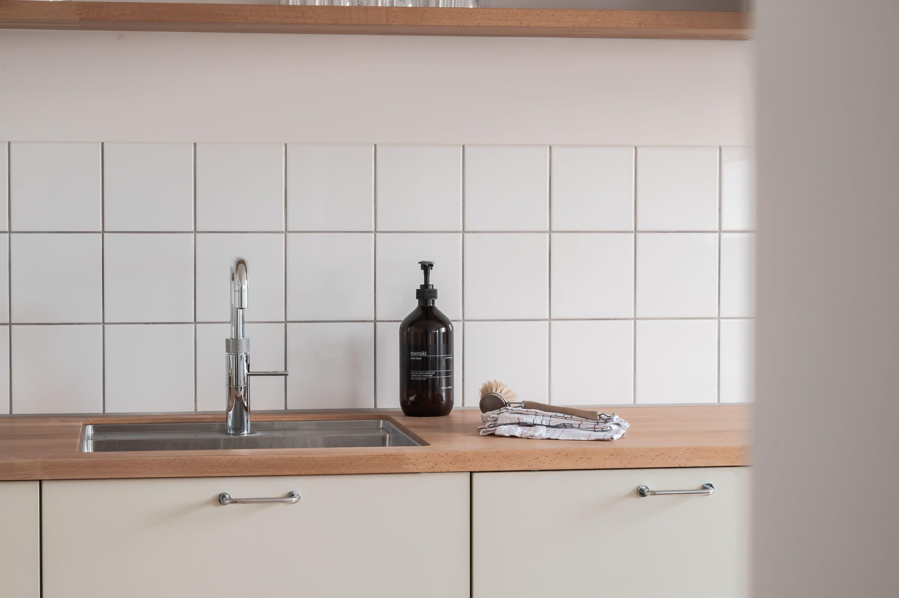 Een keuken met een spoelbak van roestvrij staal, een zwarte fles en een houten aanrecht.