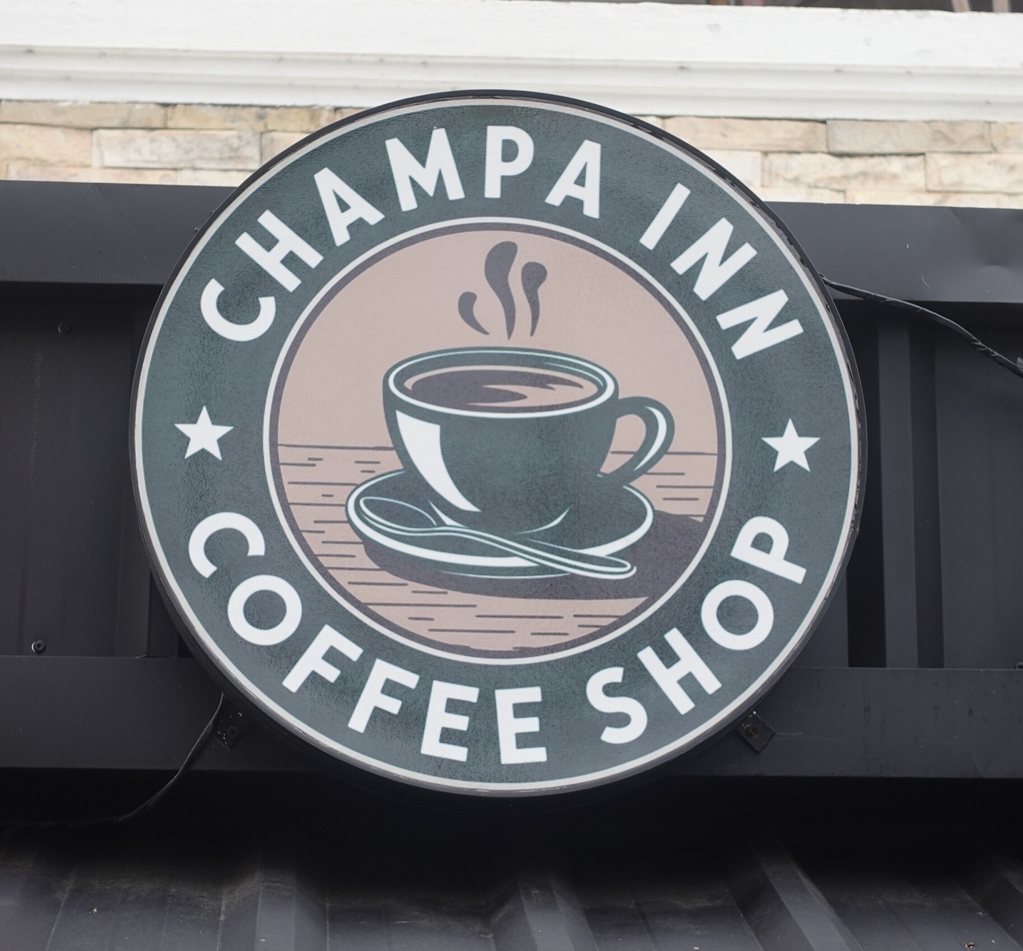 A circular sign with the text "Champa Inn Coffee Shop" and an illustration of a cup of coffee.